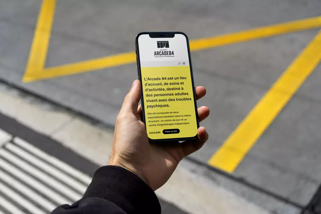visuel représentant un téléphone portable tenu d’une main avec en fond la page d’accueil du site de l’Arcade84