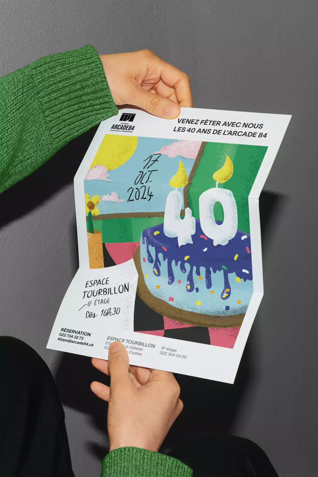 visuel représentant une affiche tenue par 2 mains. Cette affiche colorée représente un gâteau d’anniversaire pour les 40 ans de l’Arcade84