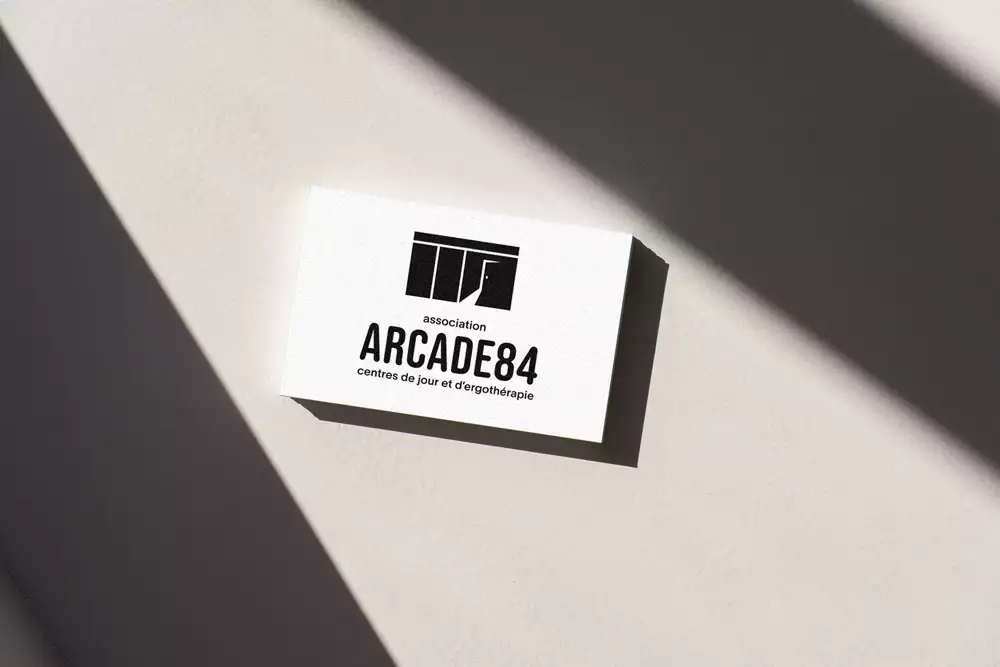visuel représentant une carte de visite posée au sol. Le logo représente une arcade (dans le sens de batiment commercial) avec une porte